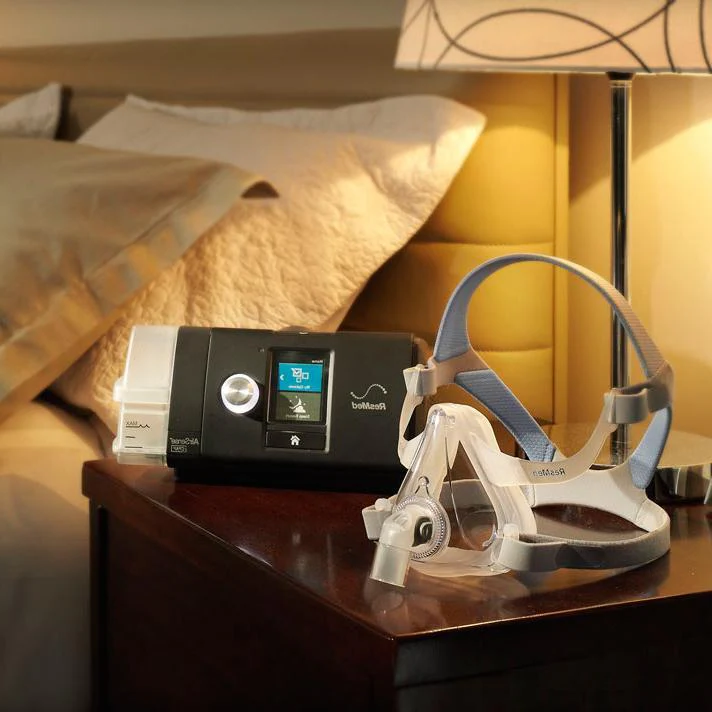 A ResMed CPAP machine and CPAP mask on a nightstand.